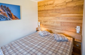 A bedroom with a wooden headboard, a bed with plaid bedding, and a painting of a mountain on the wall. - 50m from ski slopes, 1st floor, balcony, tv, 45m², Val Thorens (Val Thorens)