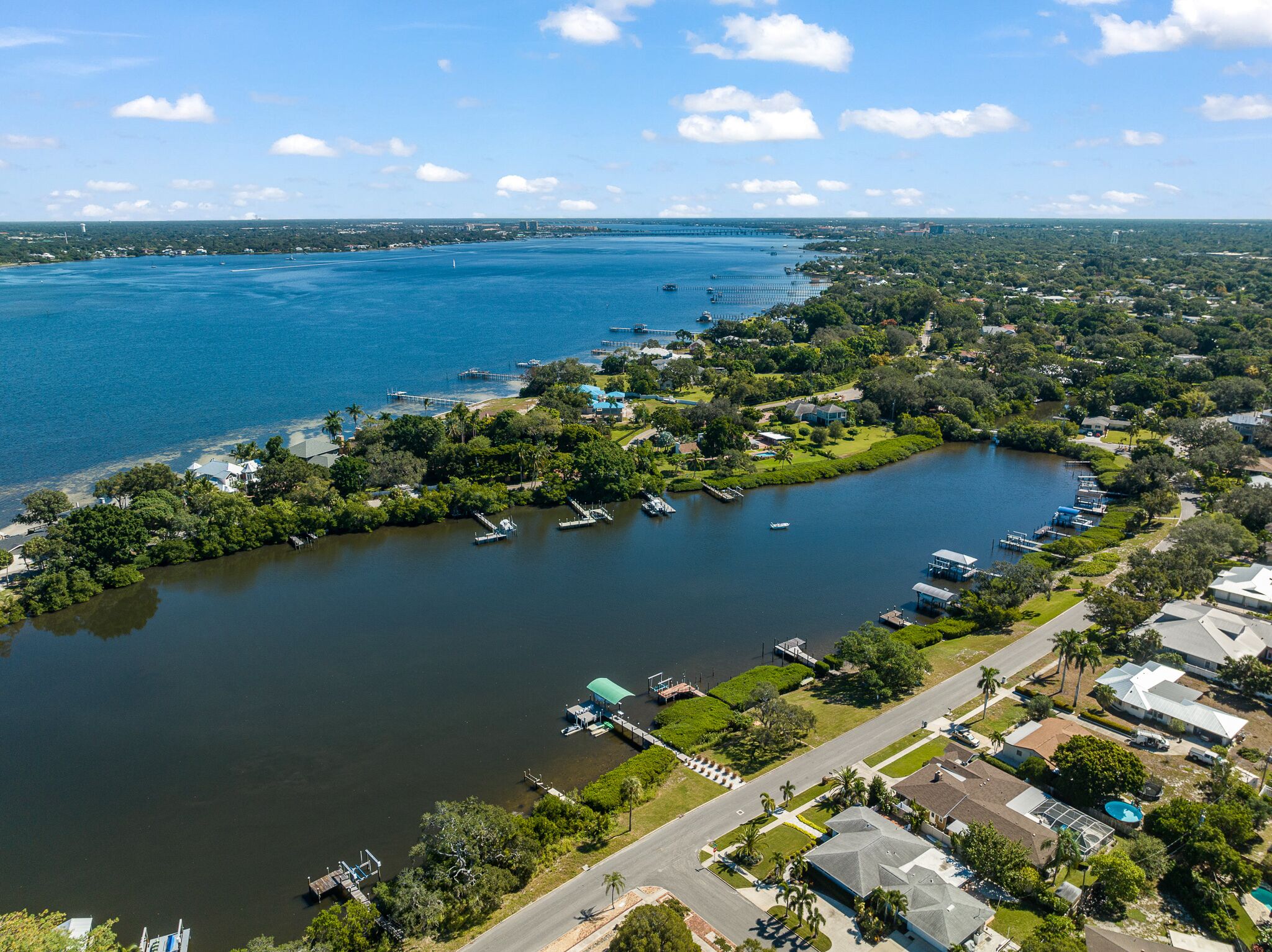 An aerial view of a coastal residential area with a marina, houses, and a bridge in the background.