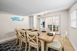 A dining area with a wooden table and chairs, a black and white patterned rug, and a wall decal of a mermaid.