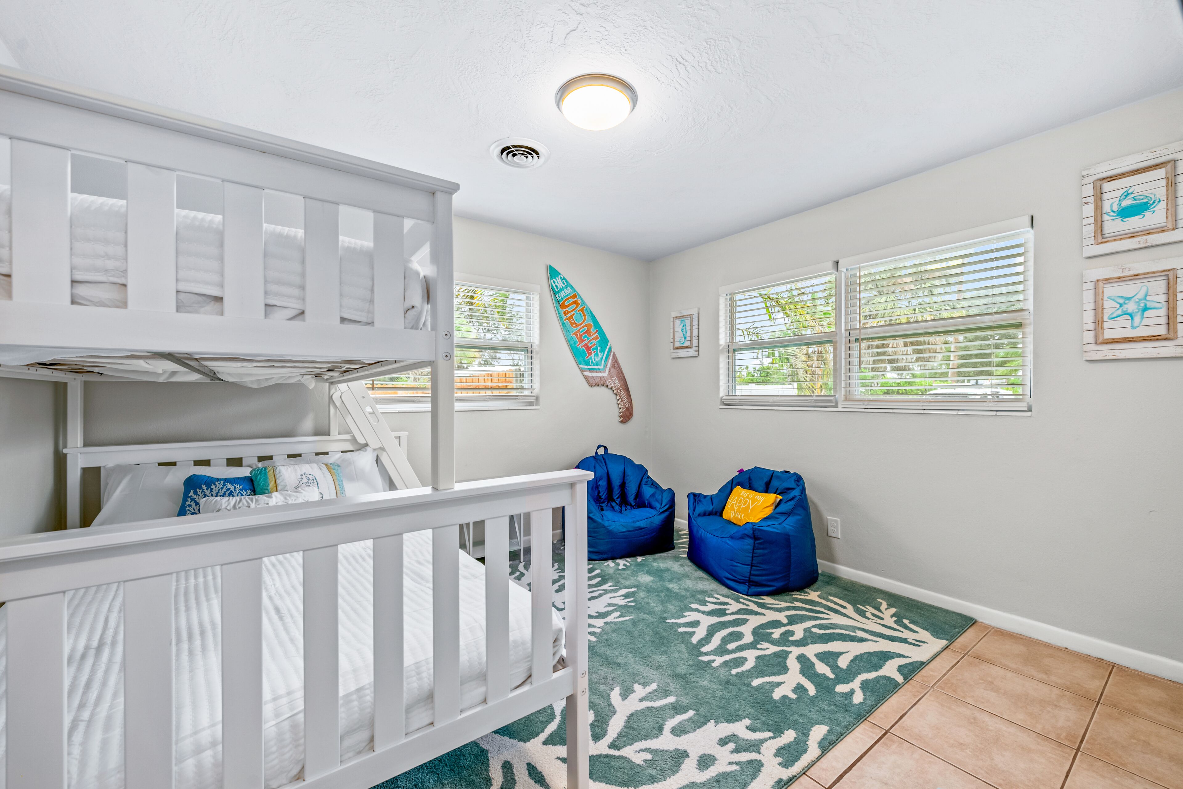 Ein Zimmer mit einem weißen Babybett, blauen Sitzsäcken, einem grün-weißen Teppich und einer Deckenleuchte.