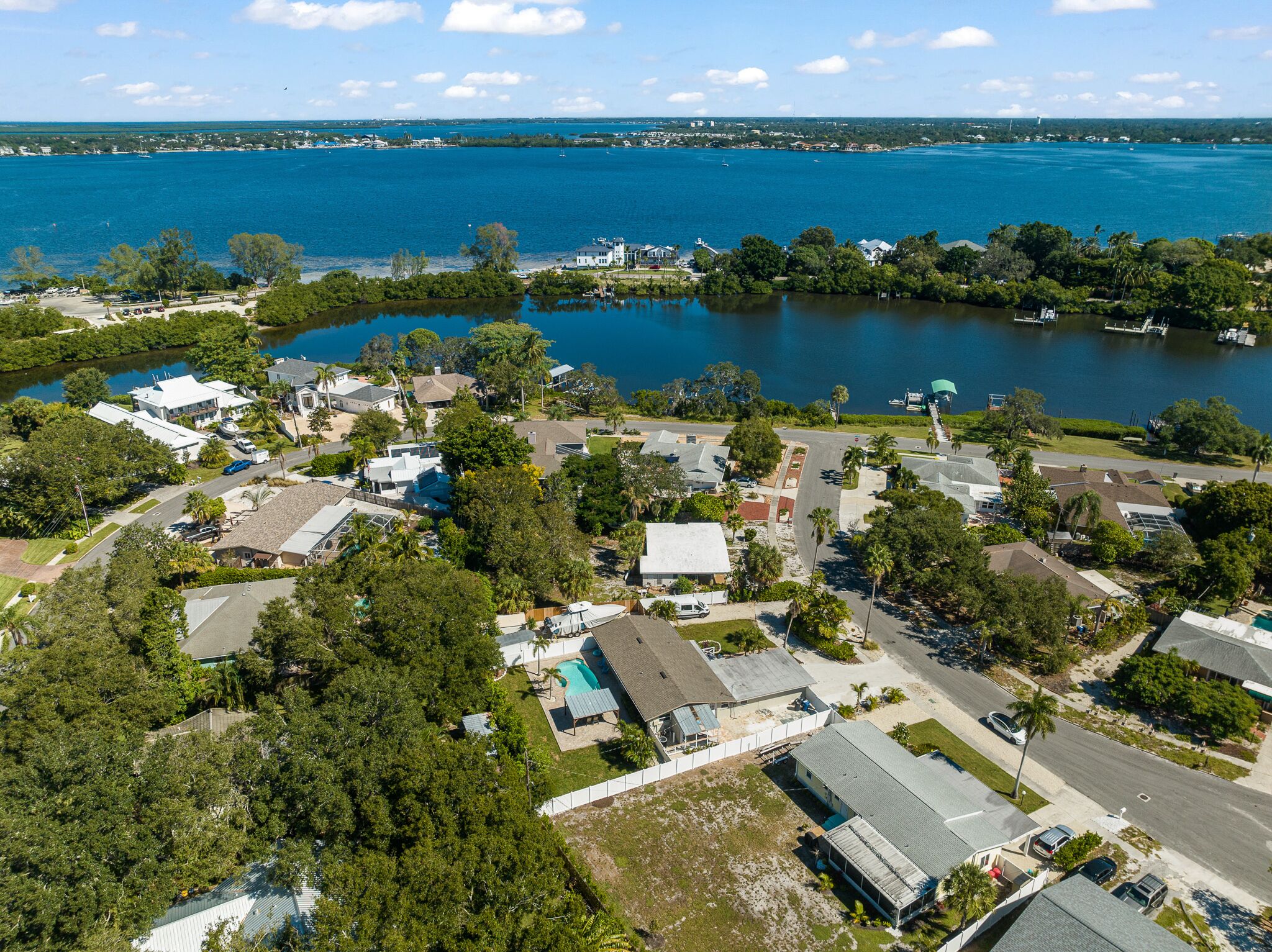 An aerial view of a residential area with houses, a swimming pool, and a large body of water.