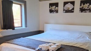 Een net opgemaakt bed met een wit en grijs dekbedovertrek, een opgevouwen handdoek en een raam met gordijnen.