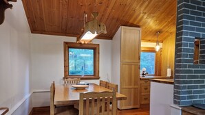 Een houten eettafel met stoelen, een raam met uitzicht op bomen, een keuken met een bakstenen muur en houten kastjes.