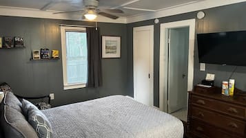 Quarto com cama, cômoda, ventilador de teto, janela com cortinas e televisão de tela plana.