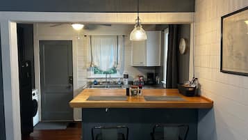 Cozinha compacta com ilha de madeira, dois banquetes, um espaço para café e um relógio na parede.