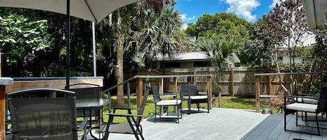 Terraza exterior con mesa y sillas, rodeada por una cerca de madera y palmeras.