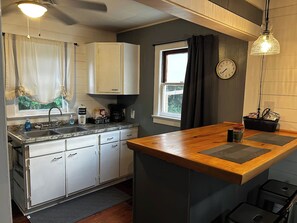 A kitchen with a wooden countertop, white cabinets, a coffee maker, and a window with curtains. - Cute cottage-historic district-hot tub (Ocala)