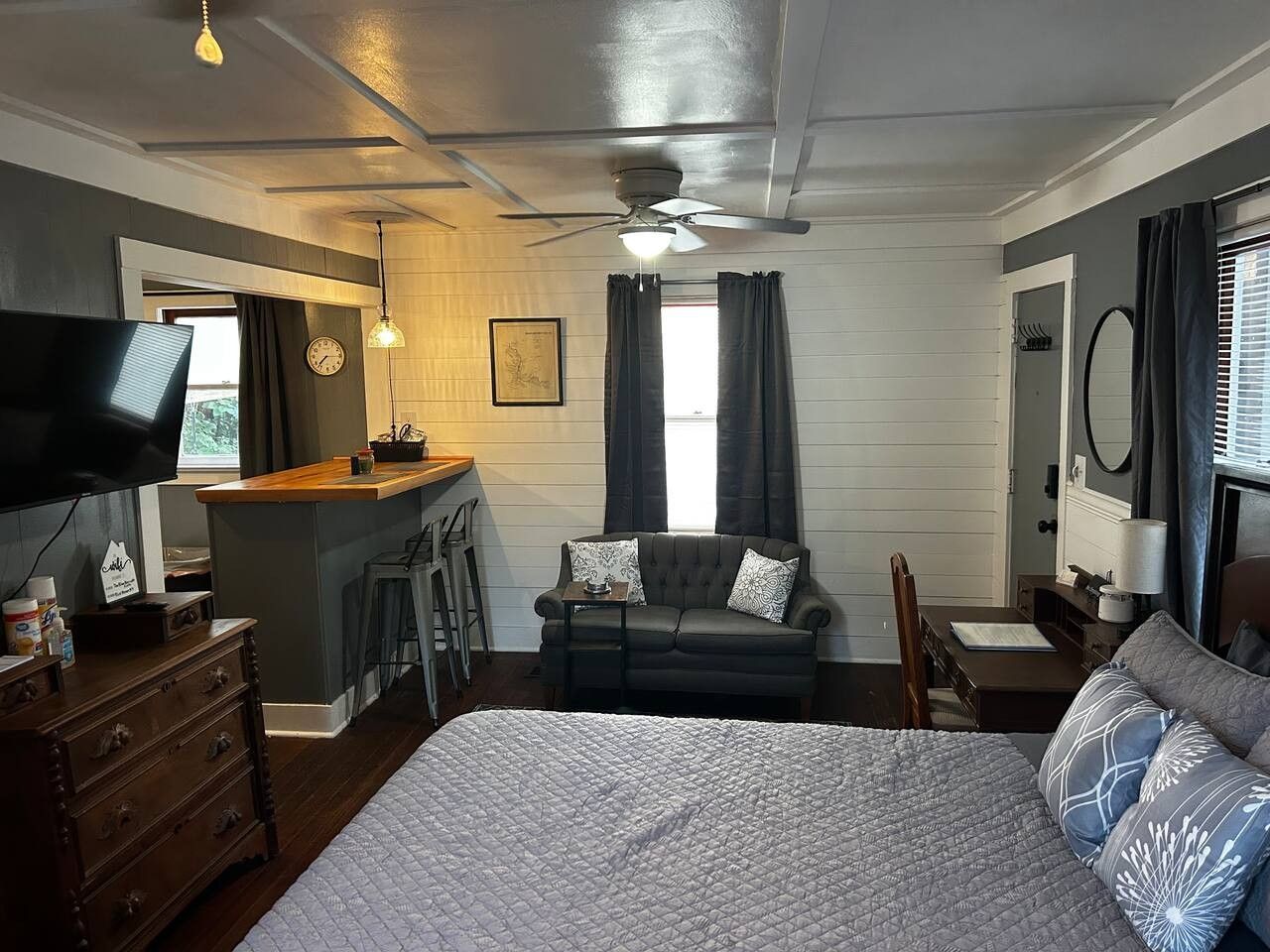 Ein Schlafzimmer mit einem Bett, einem Schreibtisch, einem Sofa, einem Fernseher und einem Deckenventilator.