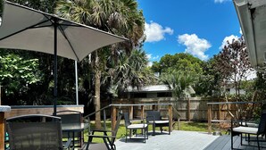 An outdoor deck with patio furniture, including chairs and a table, under a large umbrella. - Cute Cottage with Hot Tub-Historic District  (Ocala)