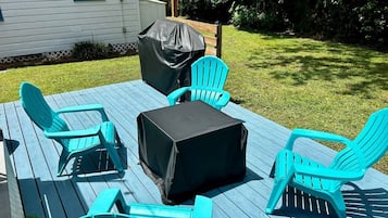 An outdoor deck with turquoise chairs and a covered table, surrounded by a grassy yard and a house.