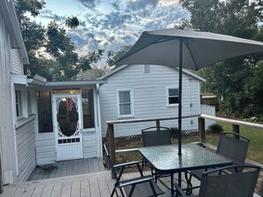 A covered patio with a table and chairs, a white house with a door, and a deck. - Morgan Cottage | Hot Tub & Historic Downtown Charm (Ocala)