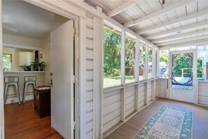 A covered porch with a view of the outdoors, a kitchen area with bar stools, and a patterned rug on the floor. - Cute cottage-historic district-hot tub (Ocala)