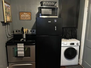 A compact kitchen with a refrigerator, oven, microwave, and washing machine.