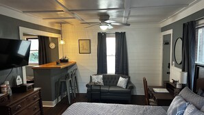 A hotel room with a bed, a sofa, a desk, a television, and a ceiling fan. - Cute Cottage with Hot Tub-Historic District  (Ocala)