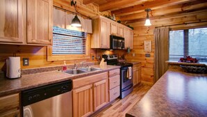 A wooden cabin kitchen with a dishwasher, sink, stove, and microwave.