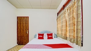 Una cama bien hecha con una colcha roja y blanca estampada, dos almohadas con la palabra “OYO” y una puerta de madera, además de una ventana con cortinas estampadas.
