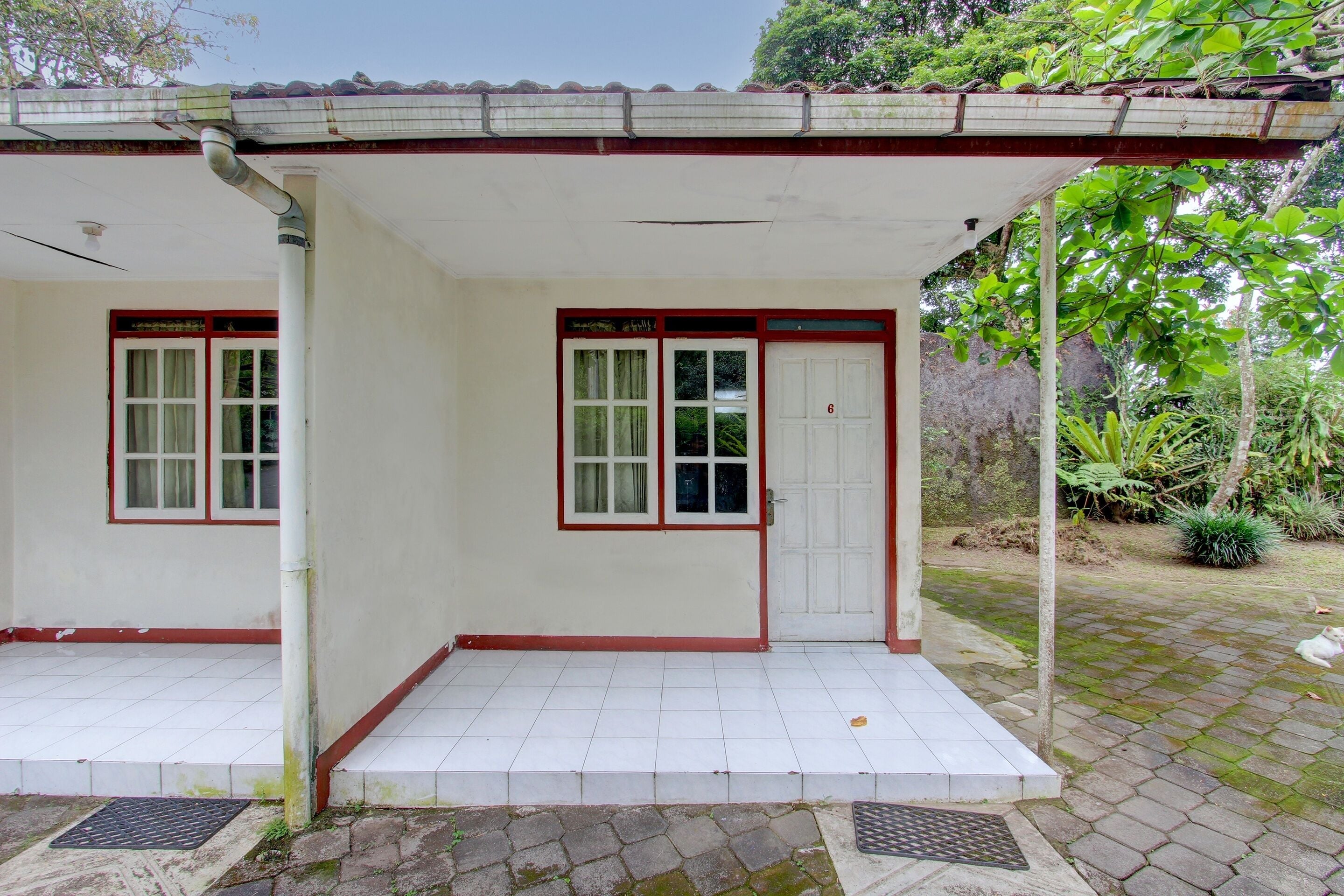 Un edificio de dos pisos con un porche cubierto, entrada de baldosas y una puerta con el número 6.