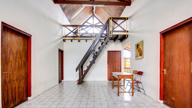 Una habitación amplia con suelo de baldosas, una escalera de madera y un comedor con mesa y sillas.