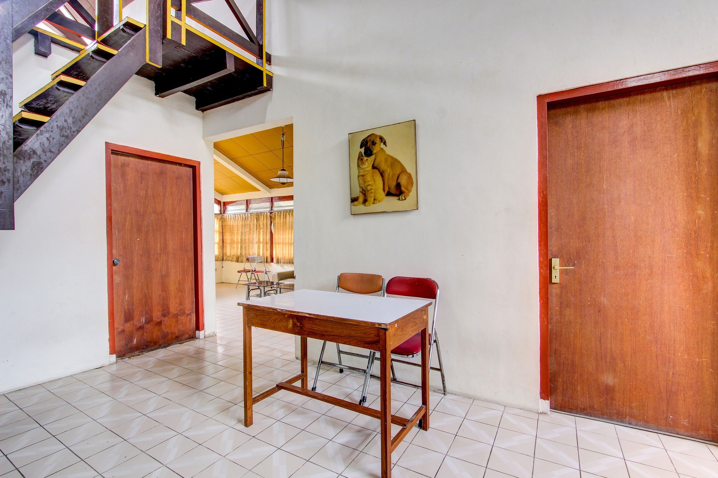 A room with a wooden table, two chairs, a wooden door, and a staircase.