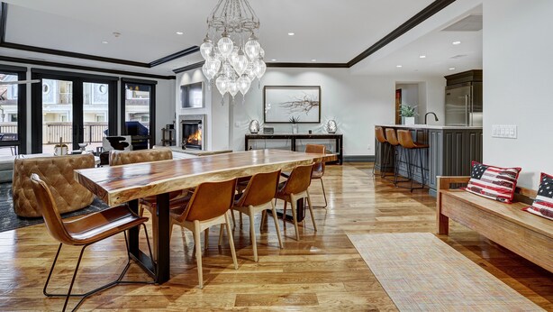 A spacious living room with a large wooden dining table, leather chairs, and a chandelier.