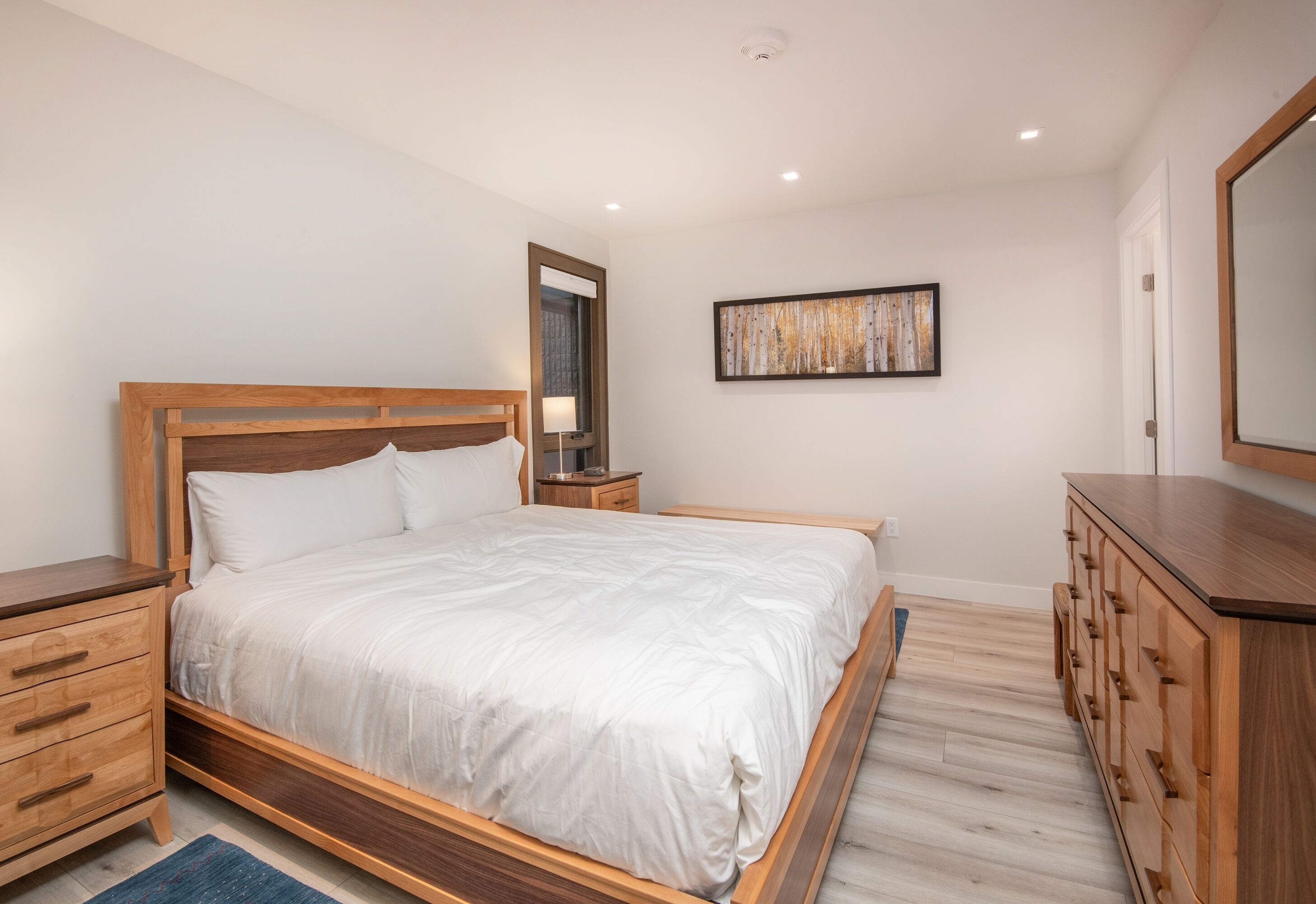 A bedroom with a wooden bed, a nightstand, a dresser, and a wall-mounted mirror.