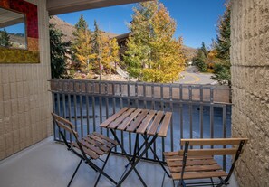 A balcony with wooden furniture, a view of trees and a building in the background. - Vail 21 #304 1 Bedroom Condo by RedAwning (Vail)