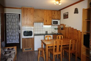 Kompakti keittiö, jossa on puiset kaapit, mikroaaltouuni, pesuallas ja ruokapöytä tuoleineen.