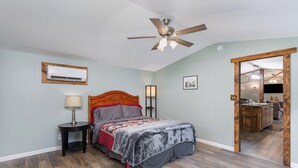 Quarto com cama, ventoinha no teto, ar condicionado e vista para a cozinha.