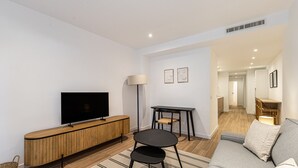 A modern living room with a flat-screen TV, wooden console, black round table, and grey sofa.