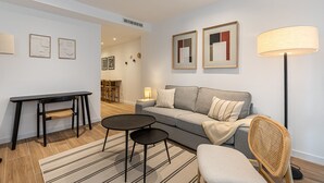 A modern living room with a grey sofa, two black tables, a wicker chair, and a floor lamp.