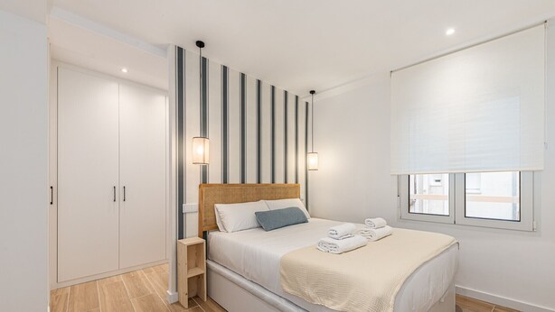 A modern bedroom with a large bed, a wardrobe, a nightstand, and a window with blinds.