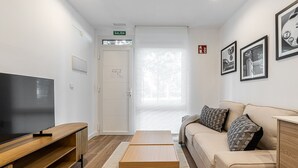 A modern living room with a flat-screen TV, wooden coffee table, beige sofa, patterned cushions, and framed pictures on the wall.