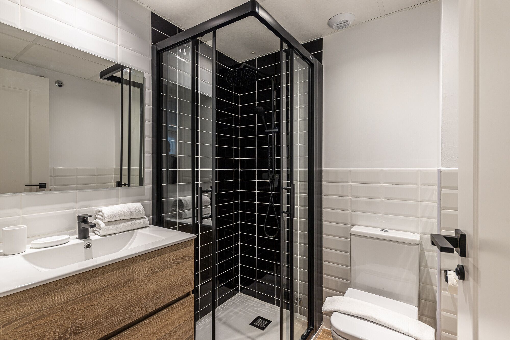 A modern bathroom with a glass-enclosed shower, a wooden vanity, and a white toilet.