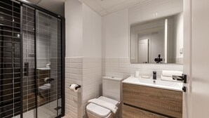 A modern bathroom with a glass shower enclosure, a toilet, a sink with a mirror, and a wooden vanity. - Waou Best IV Madrid Rio (Madrid)