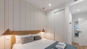 Een moderne slaapkamer met een groot bed, twee hanglampen, een houten hoofdbord en een inloopkast.