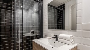 Een moderne badkamer met een grote spiegel, een wit wastafelmeubel en zwart betegelde wanden.