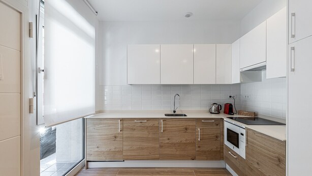Een moderne keuken met witte kastjes, een houten aanrecht, een roestvrijstalen spoelbak en een inbouwoven.