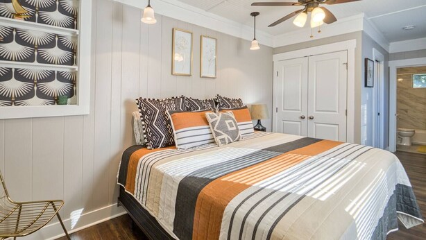 Een slaapkamer met een bed, een plafondventilator en een wandplank met decoratieve objecten.