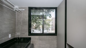A modern bathroom with a black countertop, a built-in washing machine, and a window with a view of buildings and trees. - Moderno apartamento 2 quartos (Belo Horizonte)