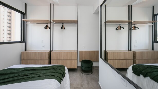 A modern bedroom with a bed, a mirror, a wardrobe, and a small stool. - Moderno apartamento 2 quartos (Belo Horizonte)