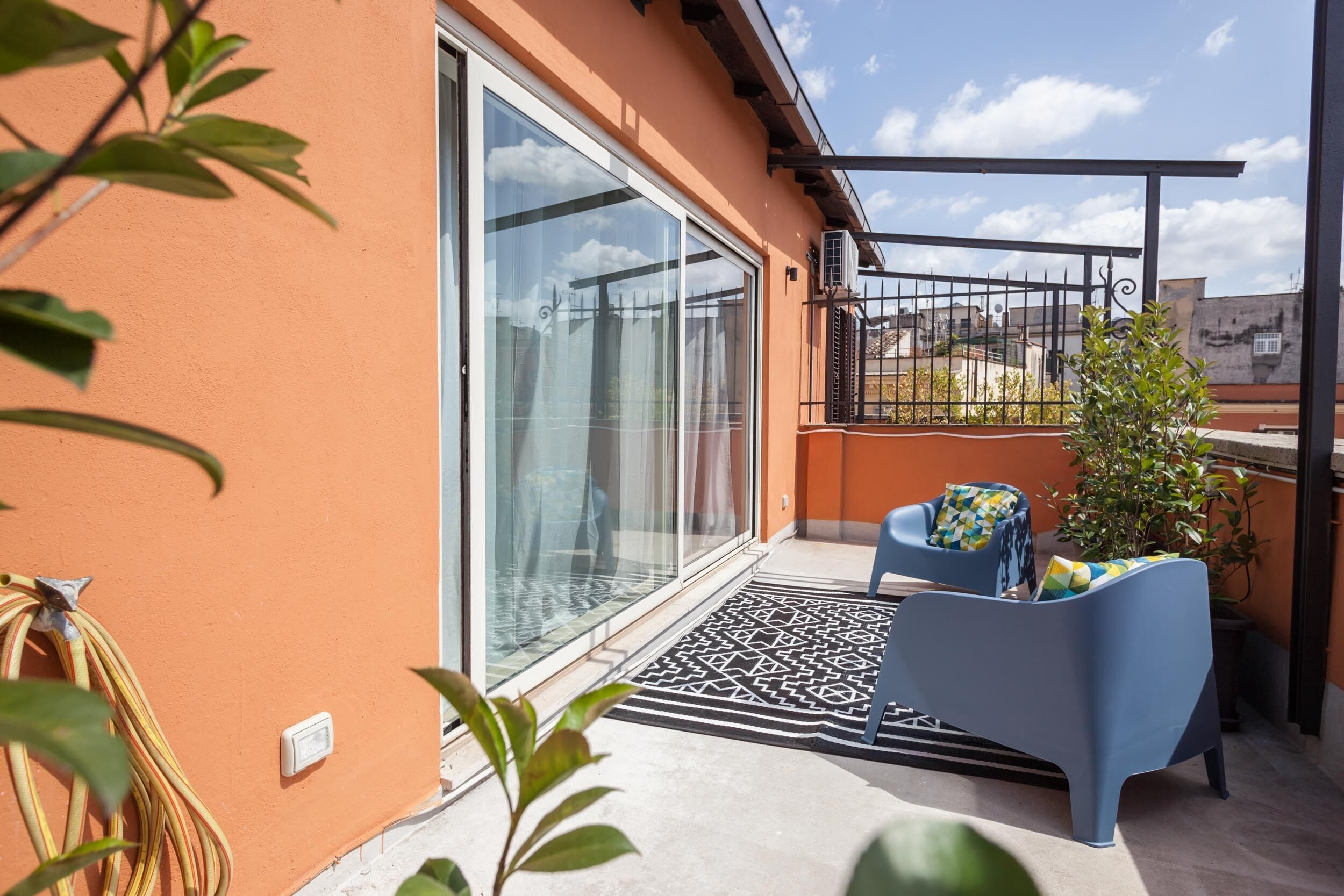 A balcony with a blue chair, a potted plant, and a glass door leading to an outdoor area.