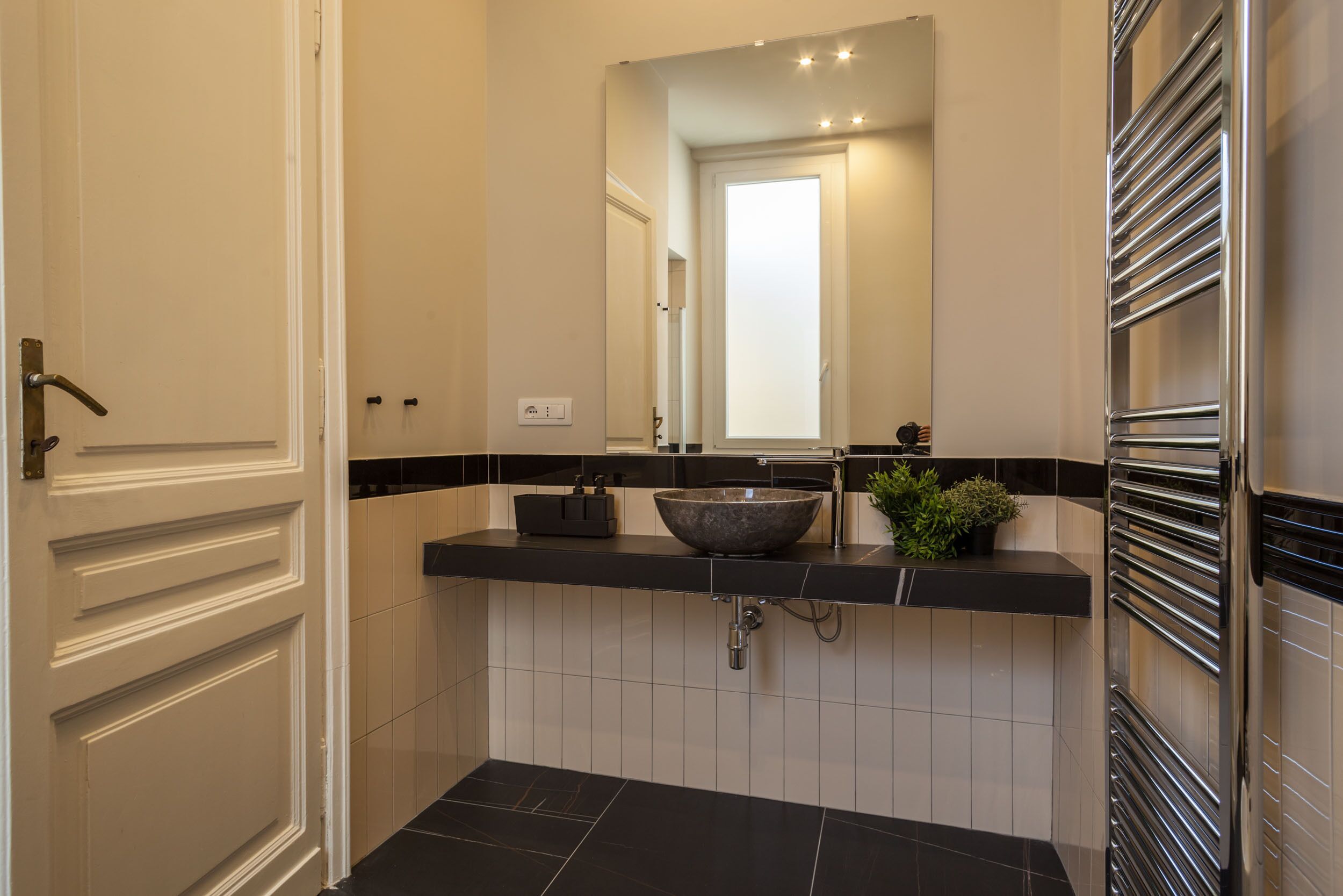 A modern bathroom with a black and white tiled backsplash, a vessel sink, a mirror above the sink, and a towel rack on the right.