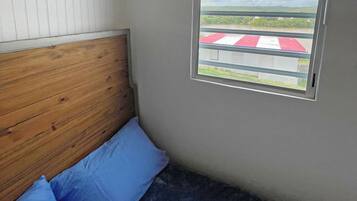 Ein Schlafzimmer mit einem hölzernen Kopfteil, einem Einzelbett mit blauer Bettwäsche und einem Fenster mit horizontalen Rollläden.
