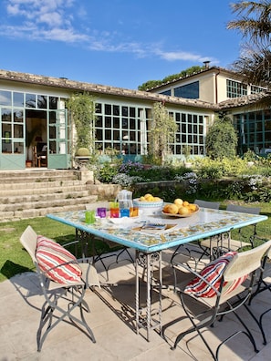 Eine Terrasse im Freien mit Esstisch, umgeben von Korbstühlen mit gestreiften Kissen.