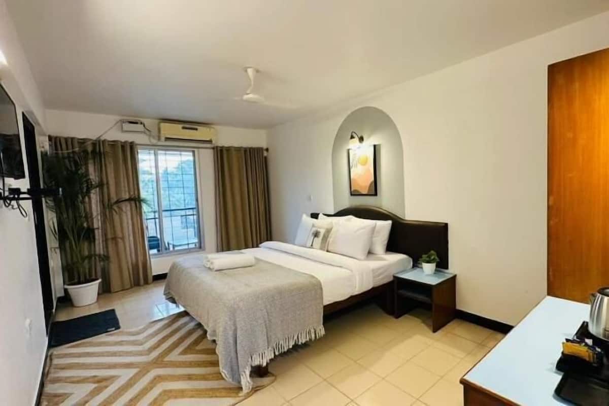 A hotel room with a bed, bedside table, and a view of the outdoors.