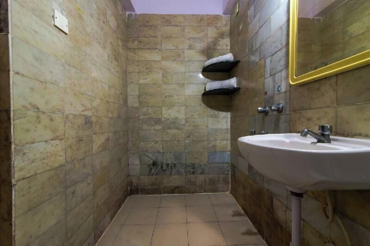 A bathroom with a white sink, a mirror with a gold frame, and a shower area with stone tiles.