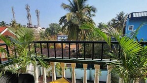 A balcony with a yellow table, potted plants, and a view of palm trees and buildings. - Olive Zip Calangute Mira by Embassy Group (Calangute)