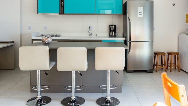Uma cozinha moderna com armários cor turquesa, uma geladeira de aço inoxidável, uma cafeteira e três banquetas.