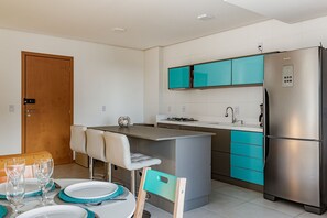 A compact kitchen with a central island, a built-in oven, and a refrigerator. - Club Vista Mar Pertinho do Beto Carrero (Penha)