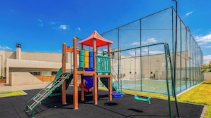 Uma área de recreação infantil com estrutura de escalada, escorregadores e espaço cercado.